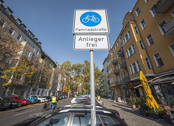 Schild "Fahrrradstraße" mit Zusatzzeichen "Radverkehr frei" von schräg unten aufgenommen. Straßenszene im Hintergrund. 