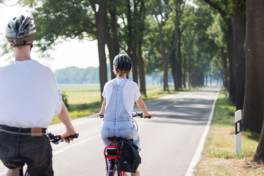 Radfahrende auf einer Landstraße Zwei Personen mit Fahrradhelmen fahren auf einer schmalen Landstraße ohne separaten Radweg.